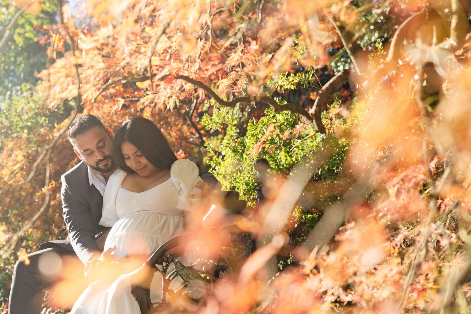 A person in white attire laughs and poses while standing against a background of sunlit autumn foliage.