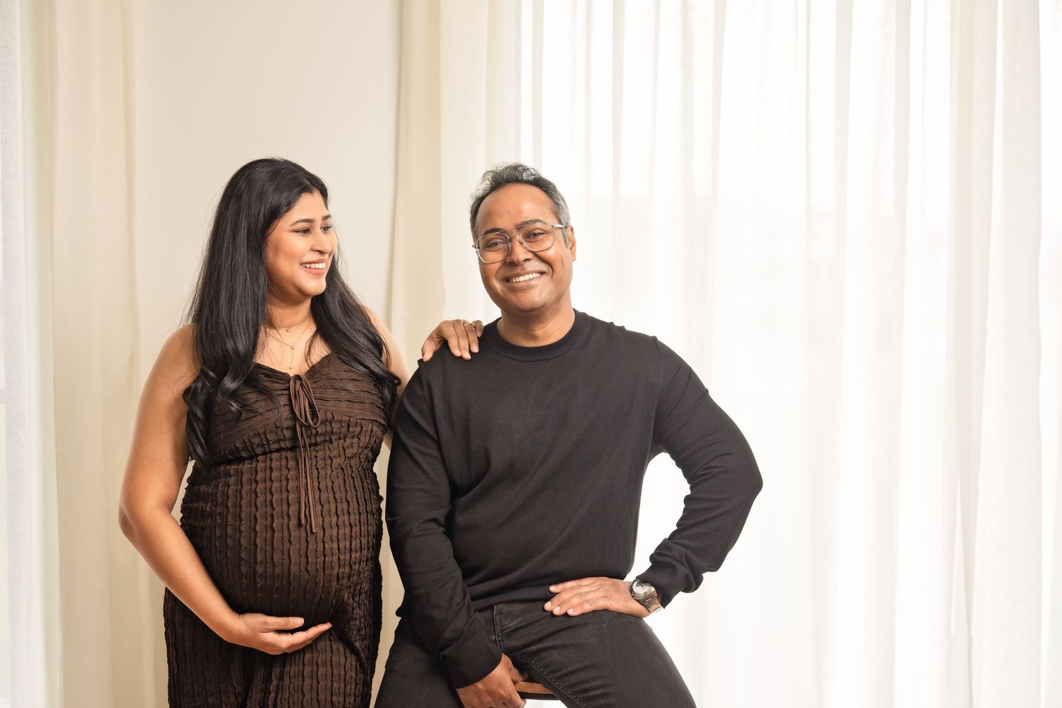 Three candid photos of a couple standing together and laughing while wearing black clothing against a white curtain.
