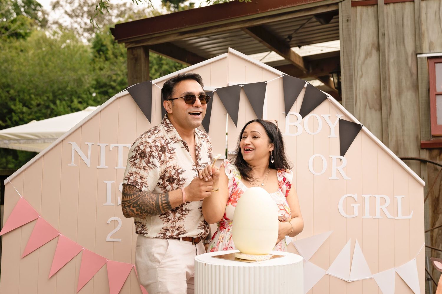 A rustic outdoor party setting with pink bunting decorations and wooden barn walls in warm sunlight.