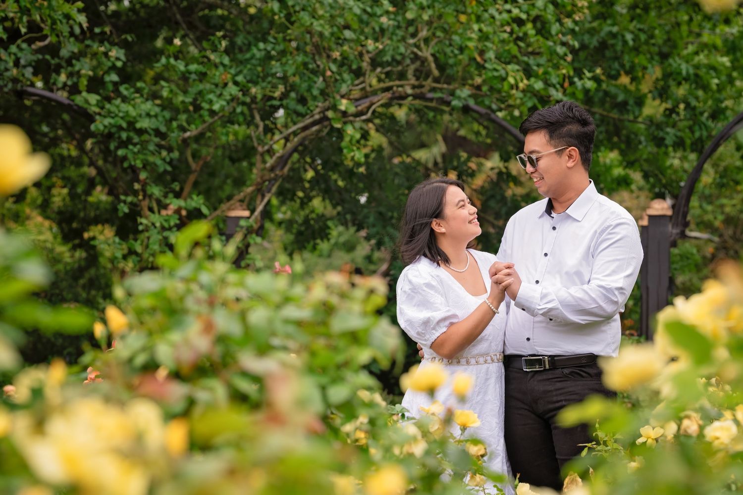 Couple sharing a romantic moment among yellow flowers and lush greenery in a garden setting.