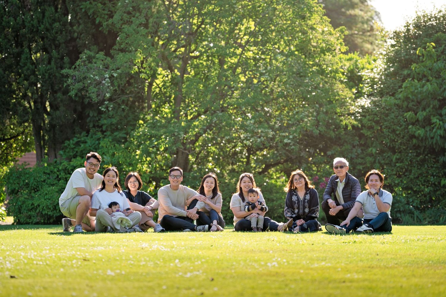 Group of people relaxing together on grassy lawn during golden hour in summer park setting.
