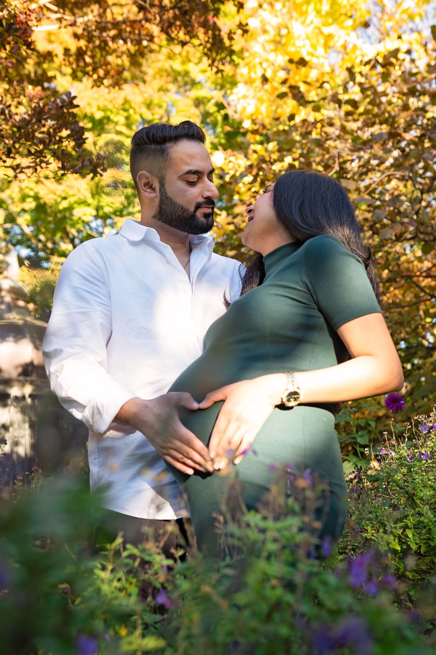 A couple shares tender moments together in a garden setting with golden sunlight filtering through autumn foliage.