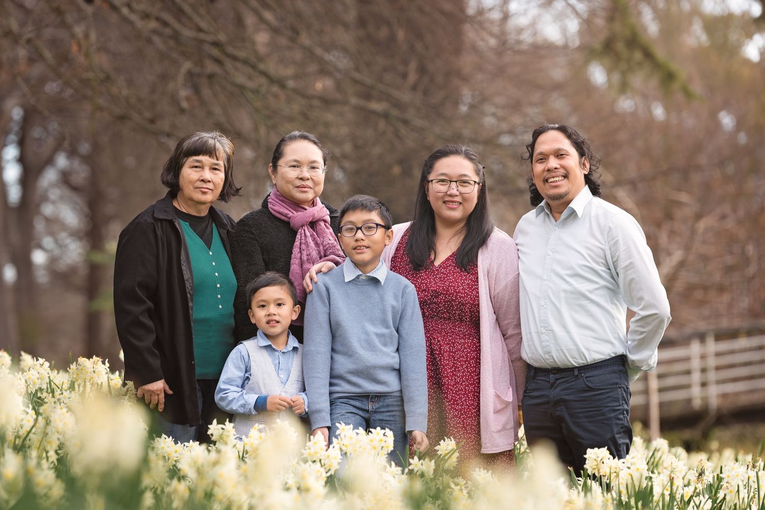 Family of six posing outdoors among white daffodils in bloom during spring.