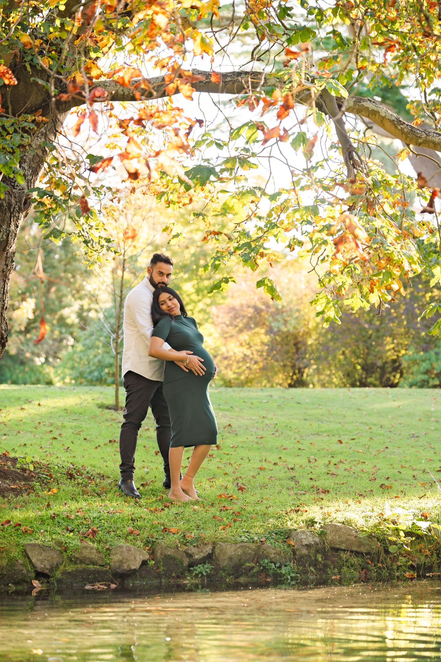 A couple sharing a romantic autumn moment by a pond surrounded by colorful fall foliage.