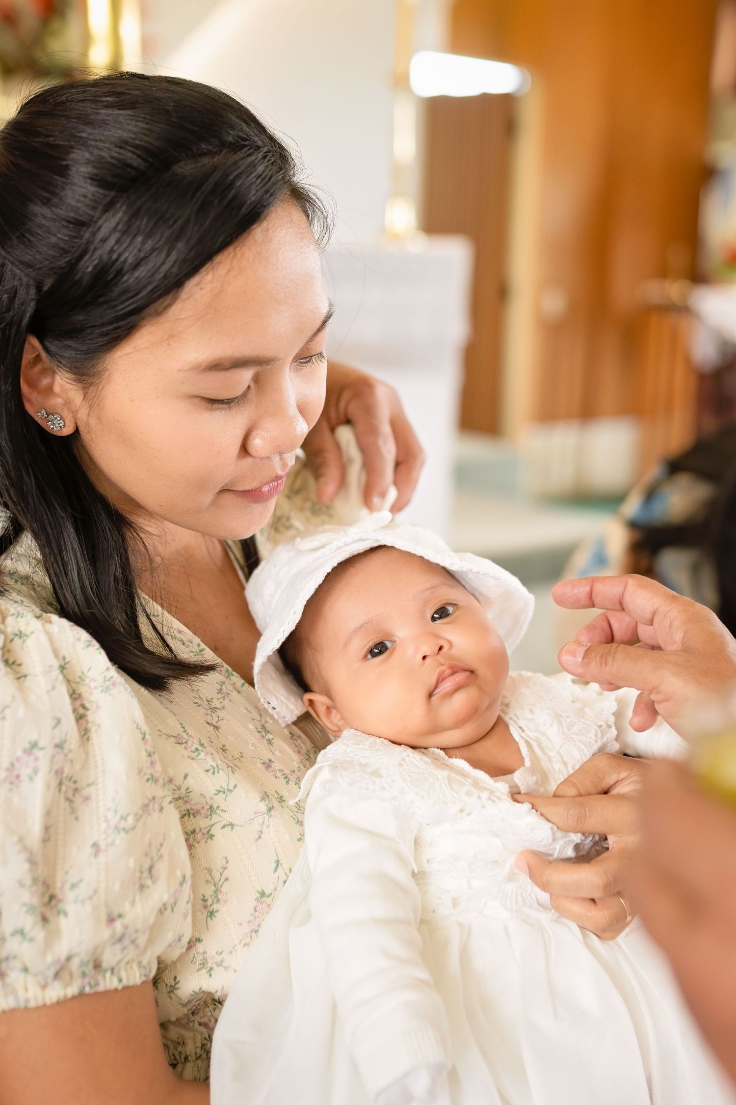 A mother holds her baby dressed in white christening gown and bonnet during a baptism ceremony.