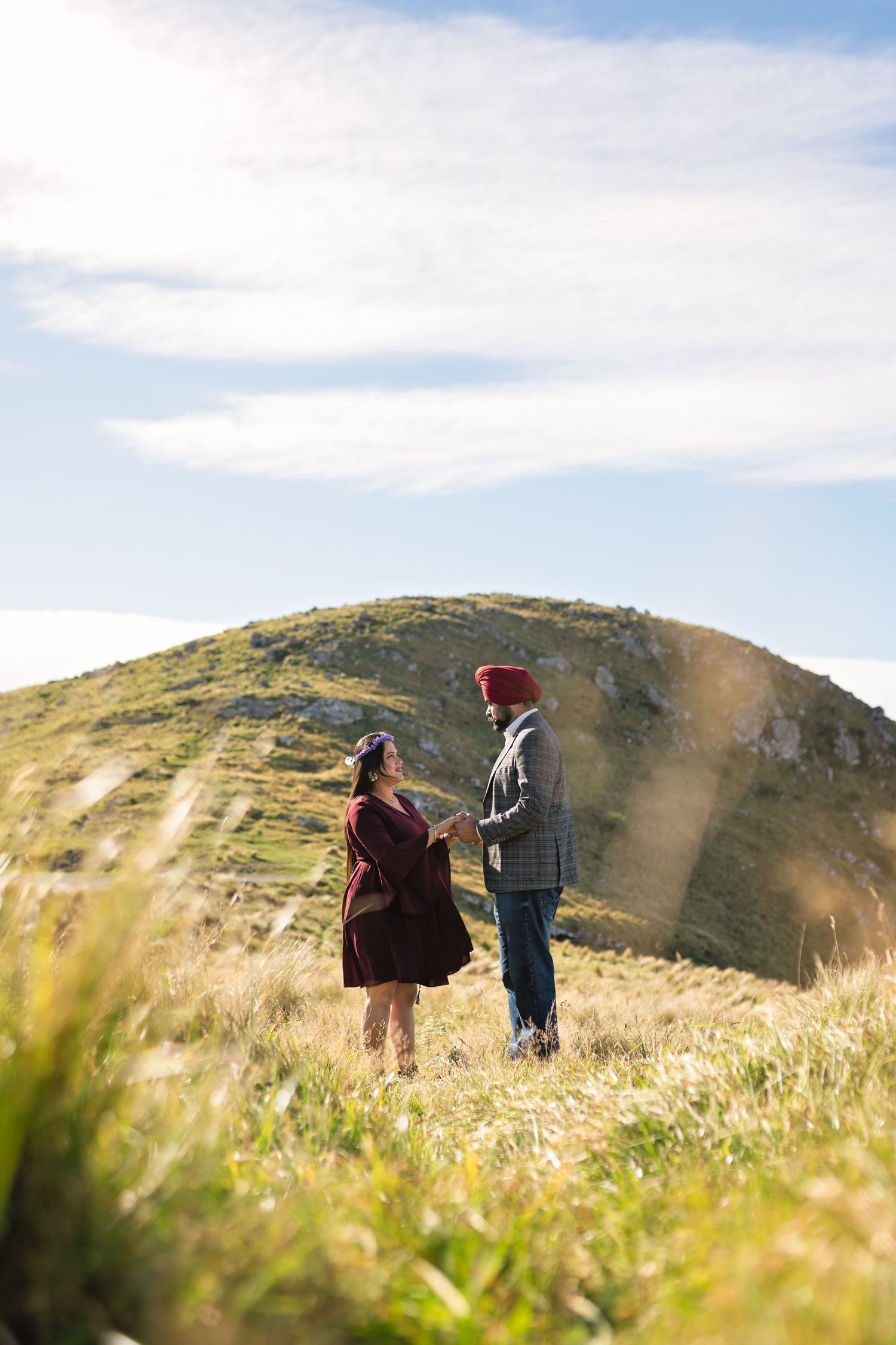 Two hikers trek across a scenic mountain ridge covered in golden grass beneath a bright blue sky on a sunny day.