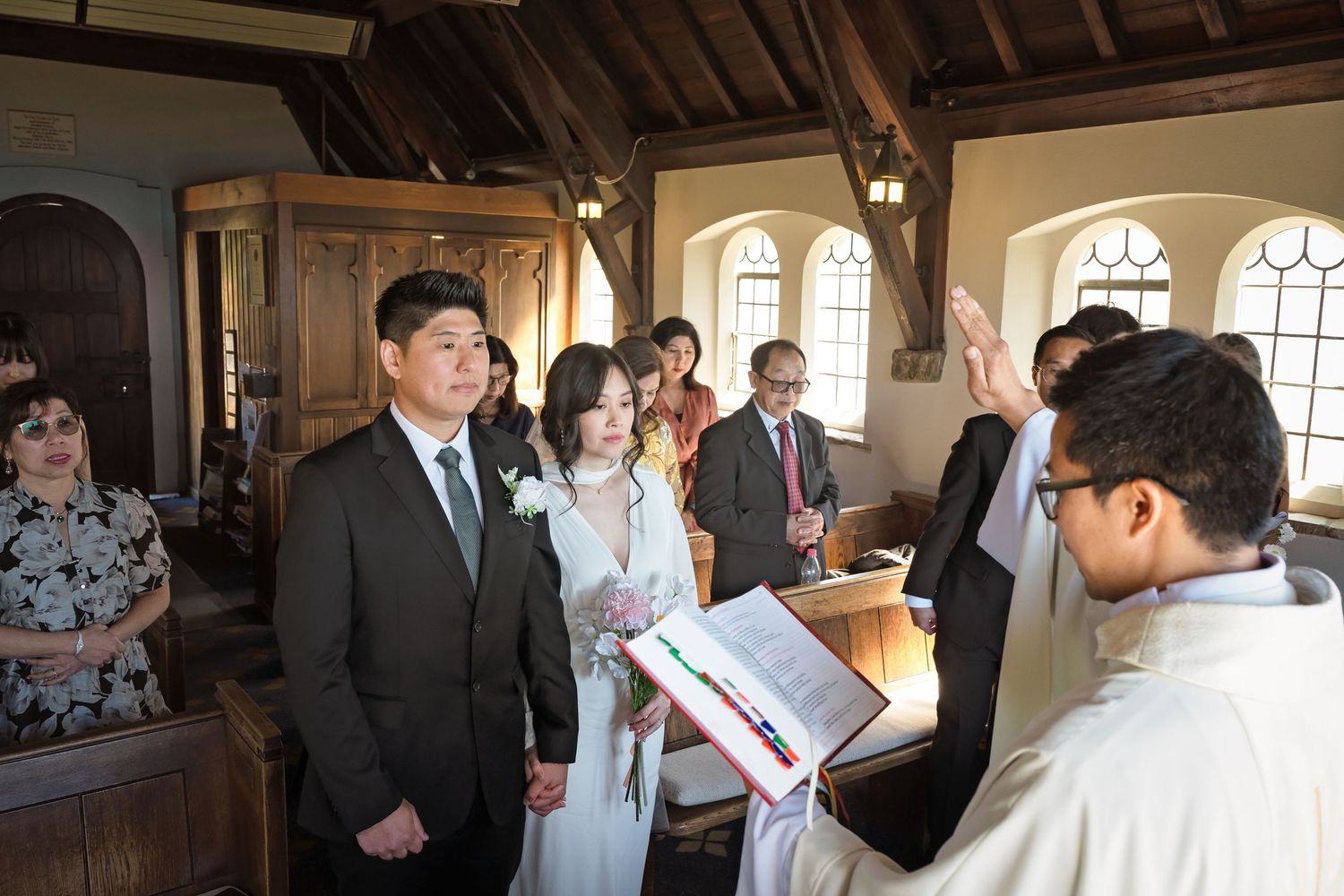 Couple exchanging vows at a church wedding ceremony with officiant raising hand in blessing.