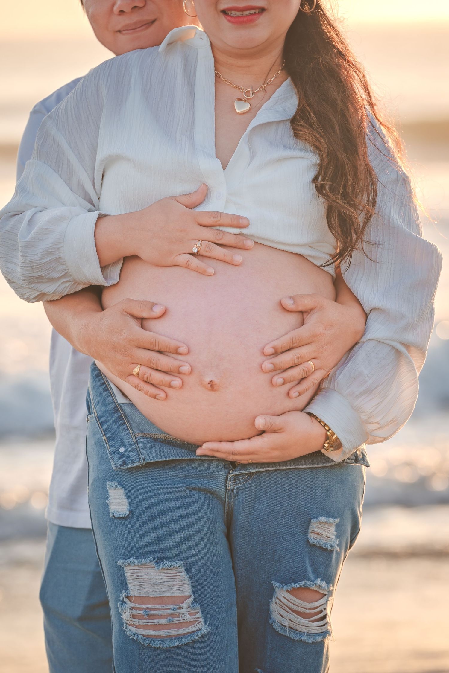 Close up of hands cradling a pregnant belly at sunset on the beach.