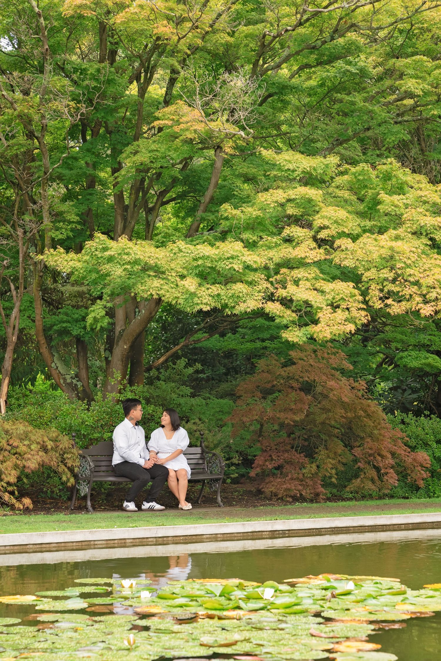Couple sitting on bench by lily pad pond surrounded by colorful autumn trees in a serene botanical garden.