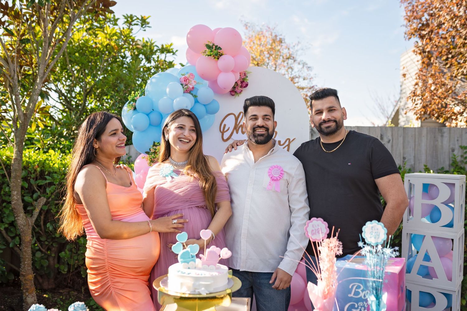 Gender reveal party celebration with pink and blue balloon decorations, tiered cake and festive backyard party setup.