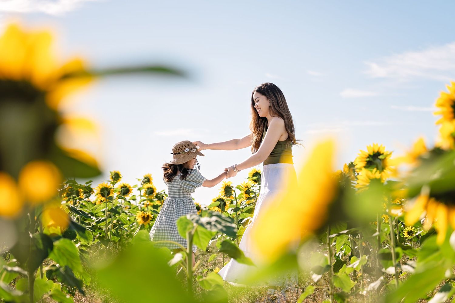A person in a white dress walks through a vibrant field of blooming yellow sunflowers on a sunny summer day.
