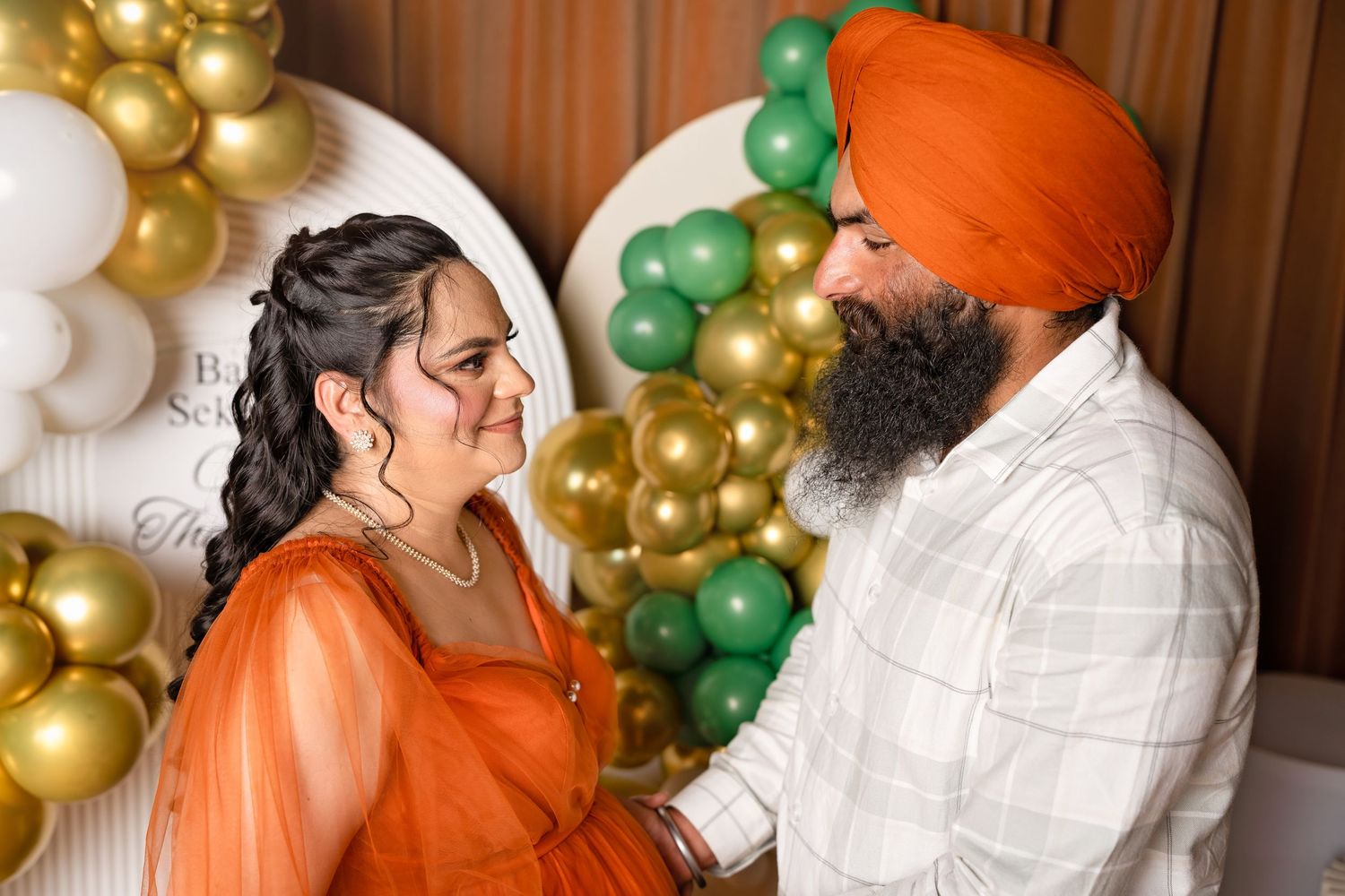 Pregnant woman in orange dress with Sikh man in orange turban at festive balloon decorated baby shower.