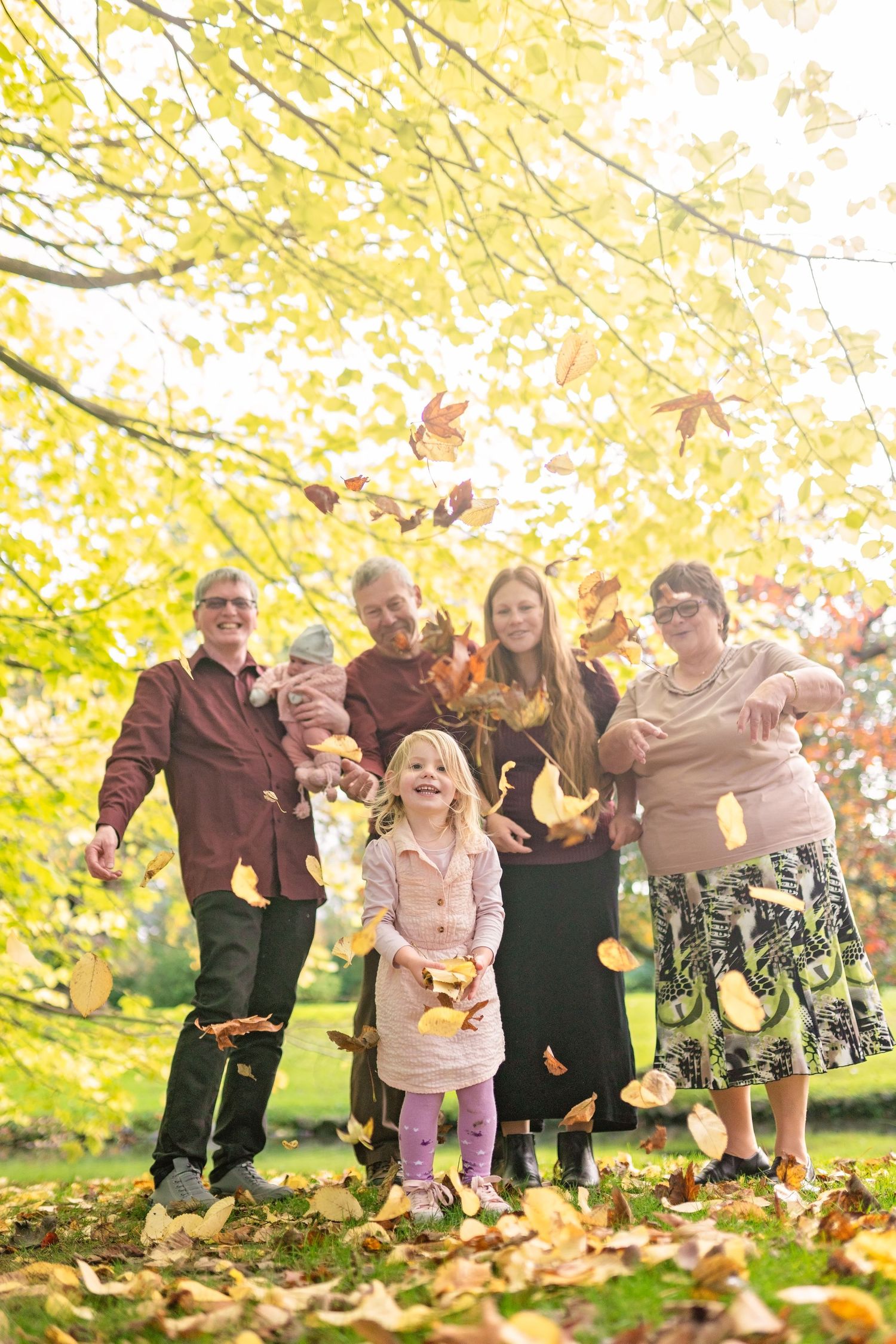 A group plays together in fallen autumn leaves under trees with golden yellow foliage on a sunny day.