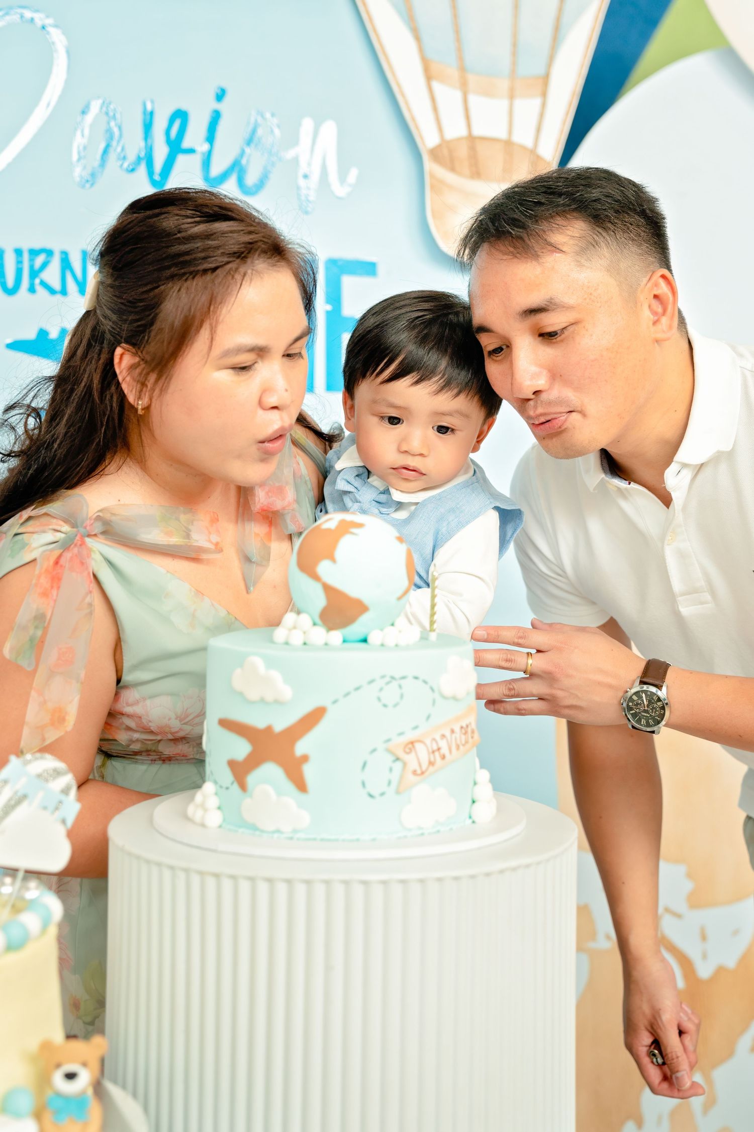 A family celebrates around a travel-themed birthday cake at a party.