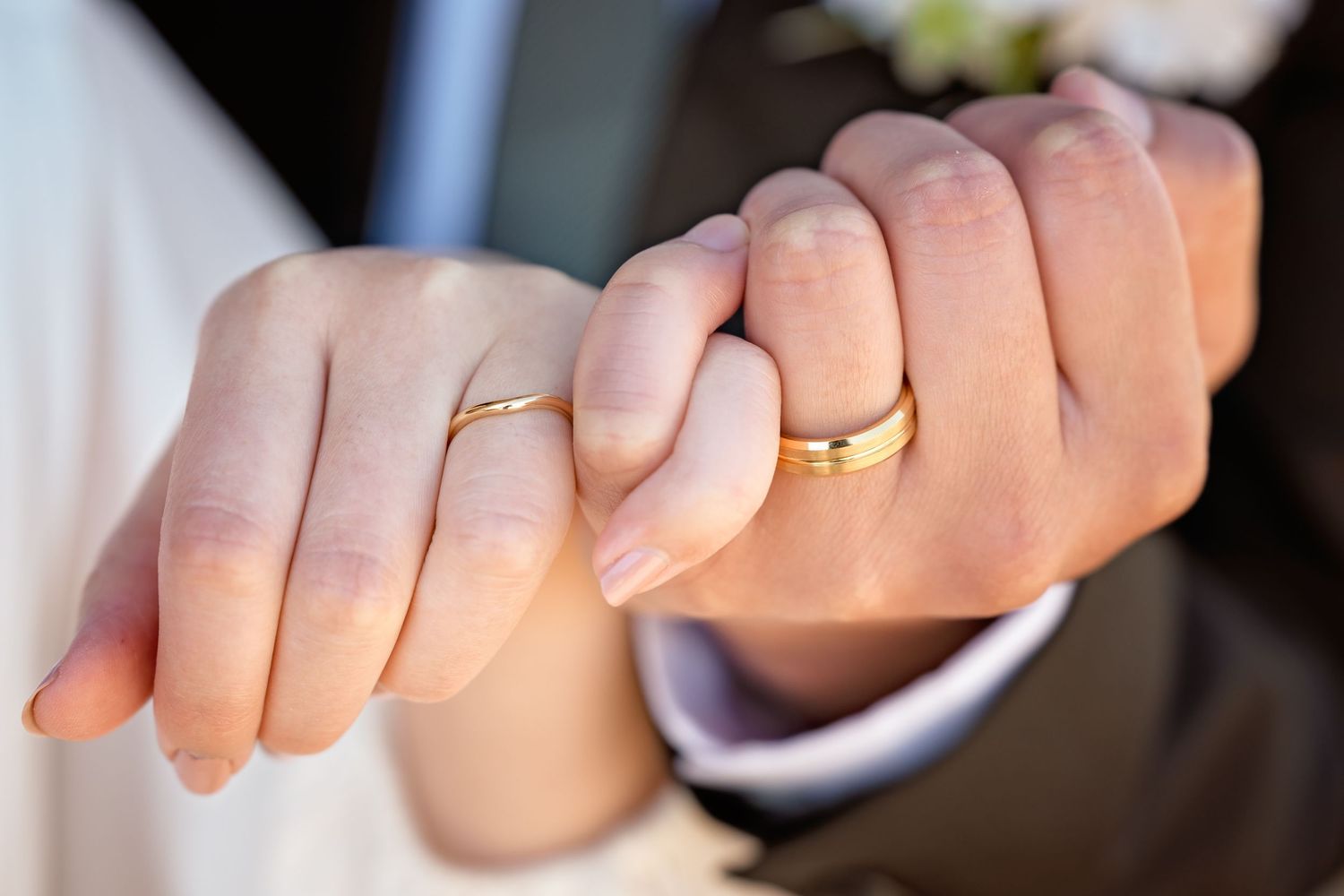 Close-up of newlywed couple holding pinkies showing matching gold wedding bands.