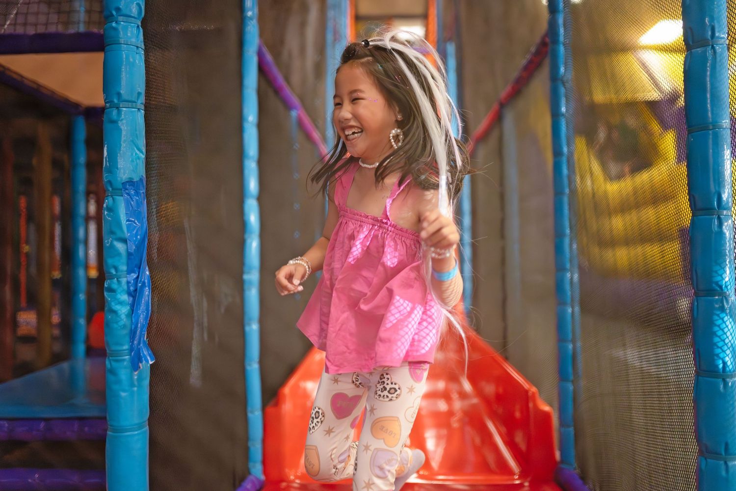 Happy young girl laughing and running in colorful indoor playground play center.