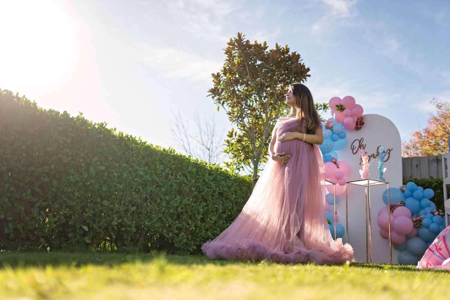 A dreamy outdoor scene with pink tulle dress near pastel balloon decorations and white furniture on a sunny lawn.