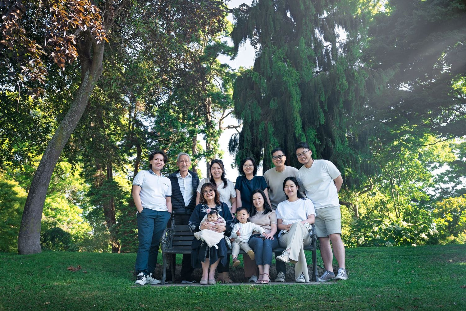 A group of people gathered on a grassy hillside for an outdoor photo session in a sunlit park setting.