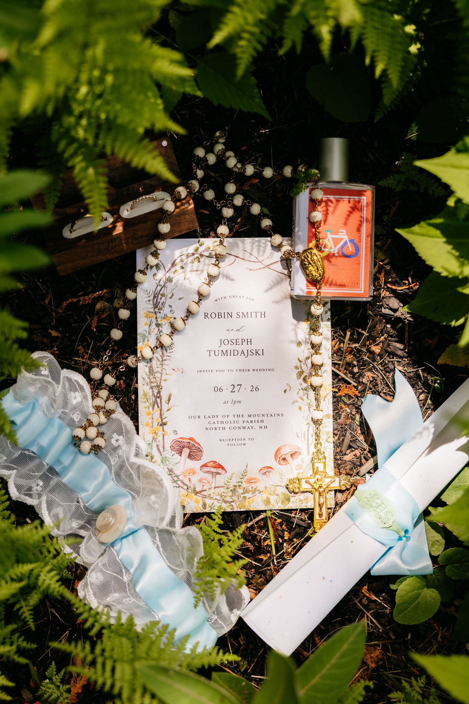 Wedding invitation for Robin Smith and Joseph Tumidajski displayed among ferns with garter, rosary, and floral accents.