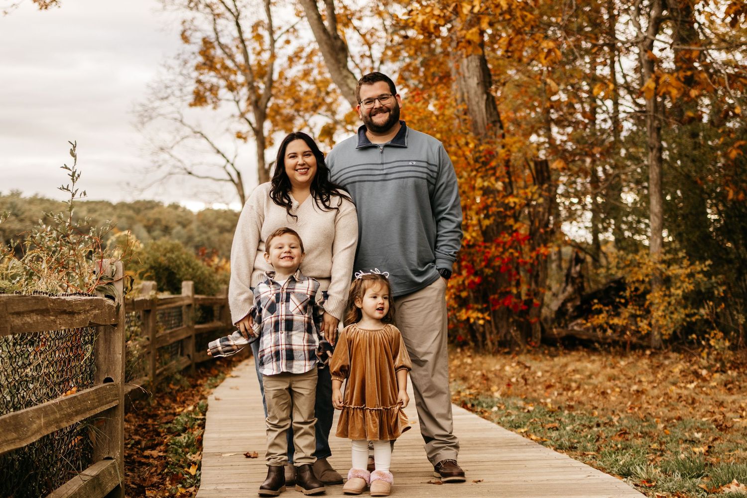 A family walks together on a path surrounded by vibrant autumn foliage in a park setting.