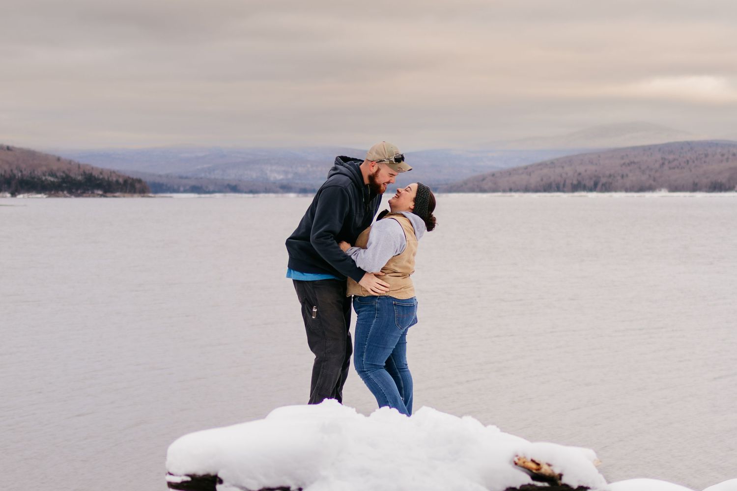 A couple embraces on a snowy mountain landscape during a winter engagement photoshoot.