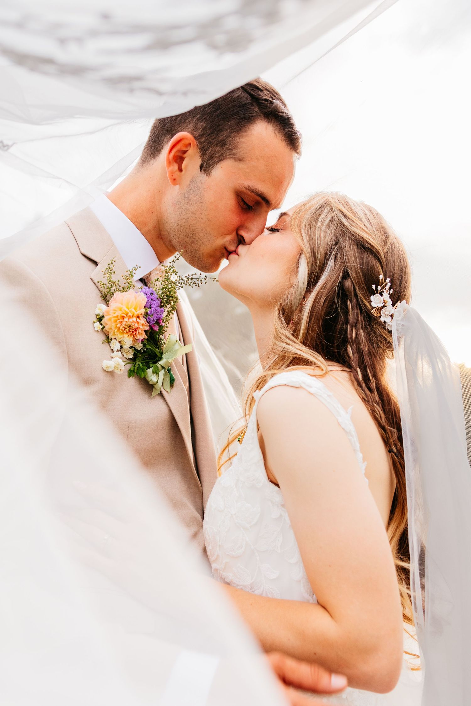 Romantic wedding couple embraces in soft dreamy lighting with floral boutonniere details.
