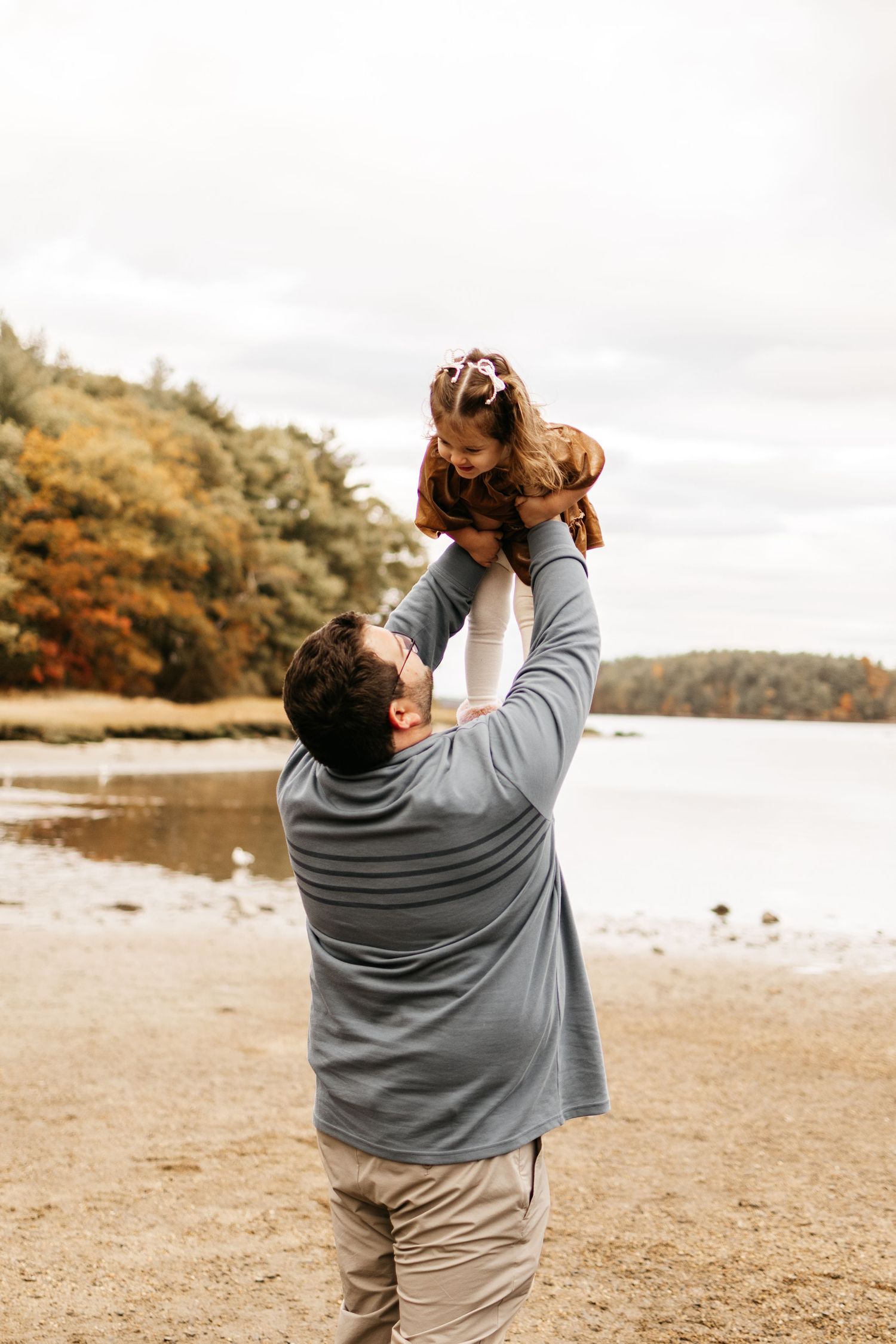 A couple shares a joyful moment together on a beach with autumn foliage in the background.