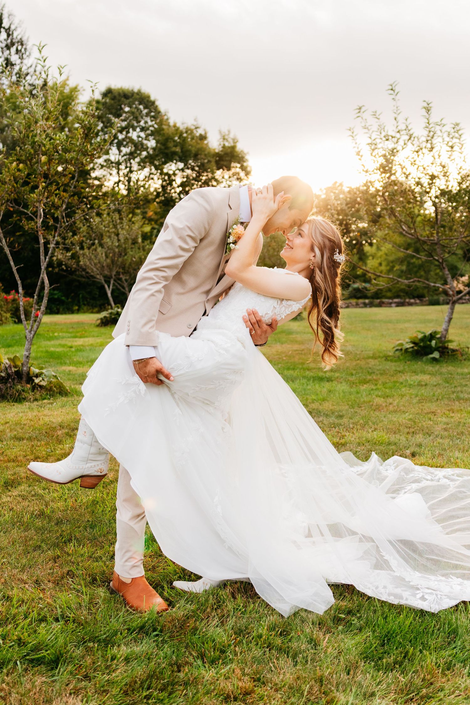 A romantic wedding couple dances in a garden at sunset with the bride's dress flowing dramatically in the breeze.