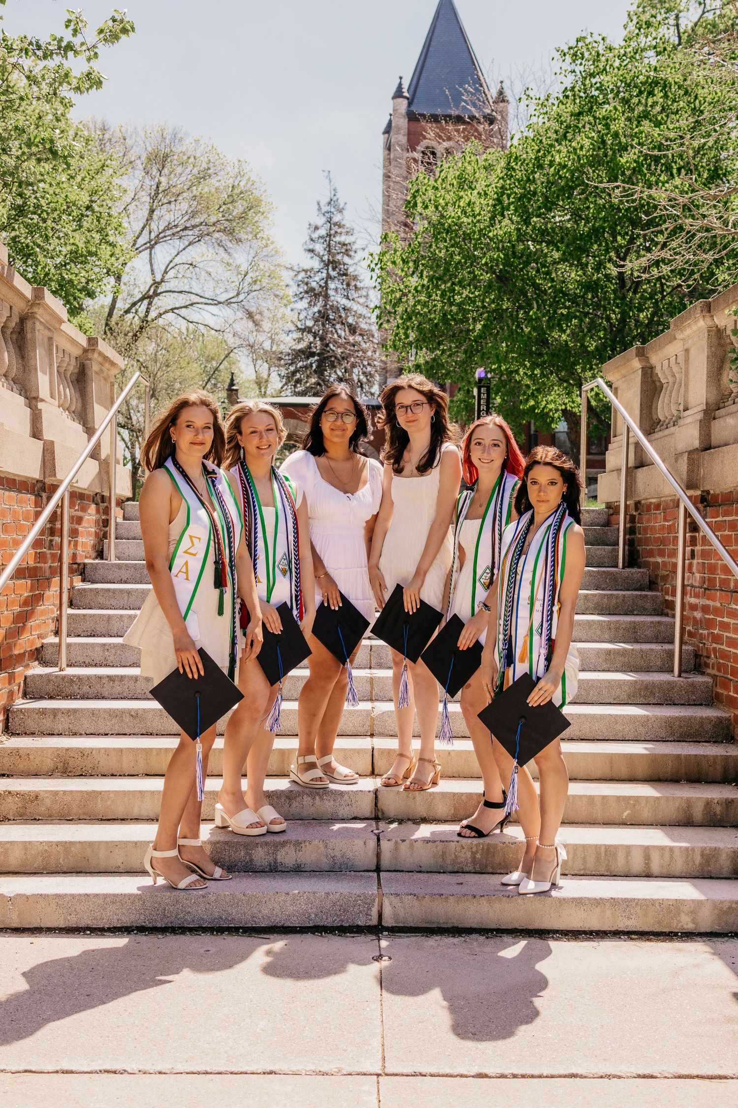 Graduates in black swimsuits and striped stoles posing playfully on stone steps.