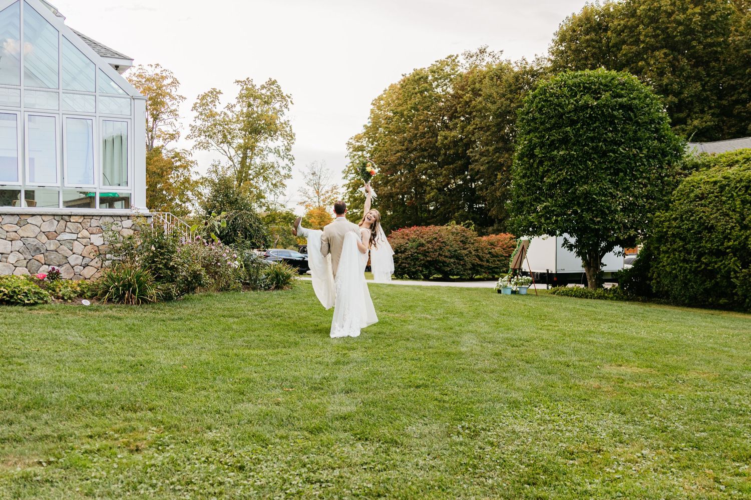 A couple in wedding attire walks hand in hand across a lush green lawn on their special day.