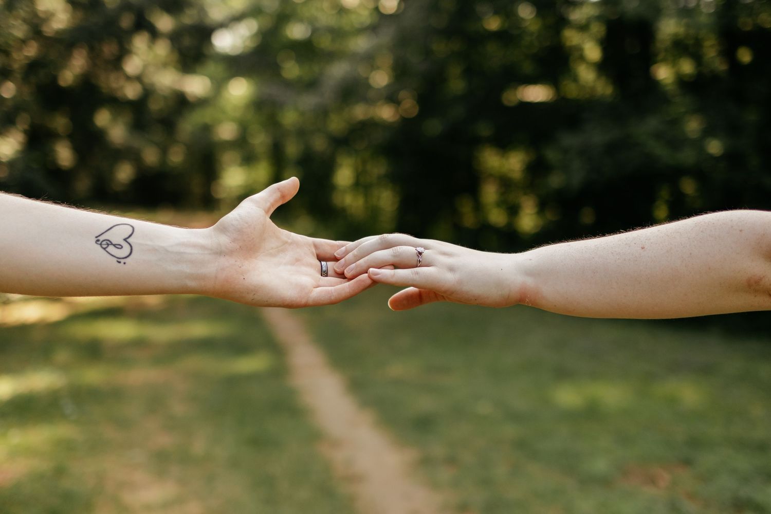Close up of hands reaching out to each other against a blurred natural outdoor background.