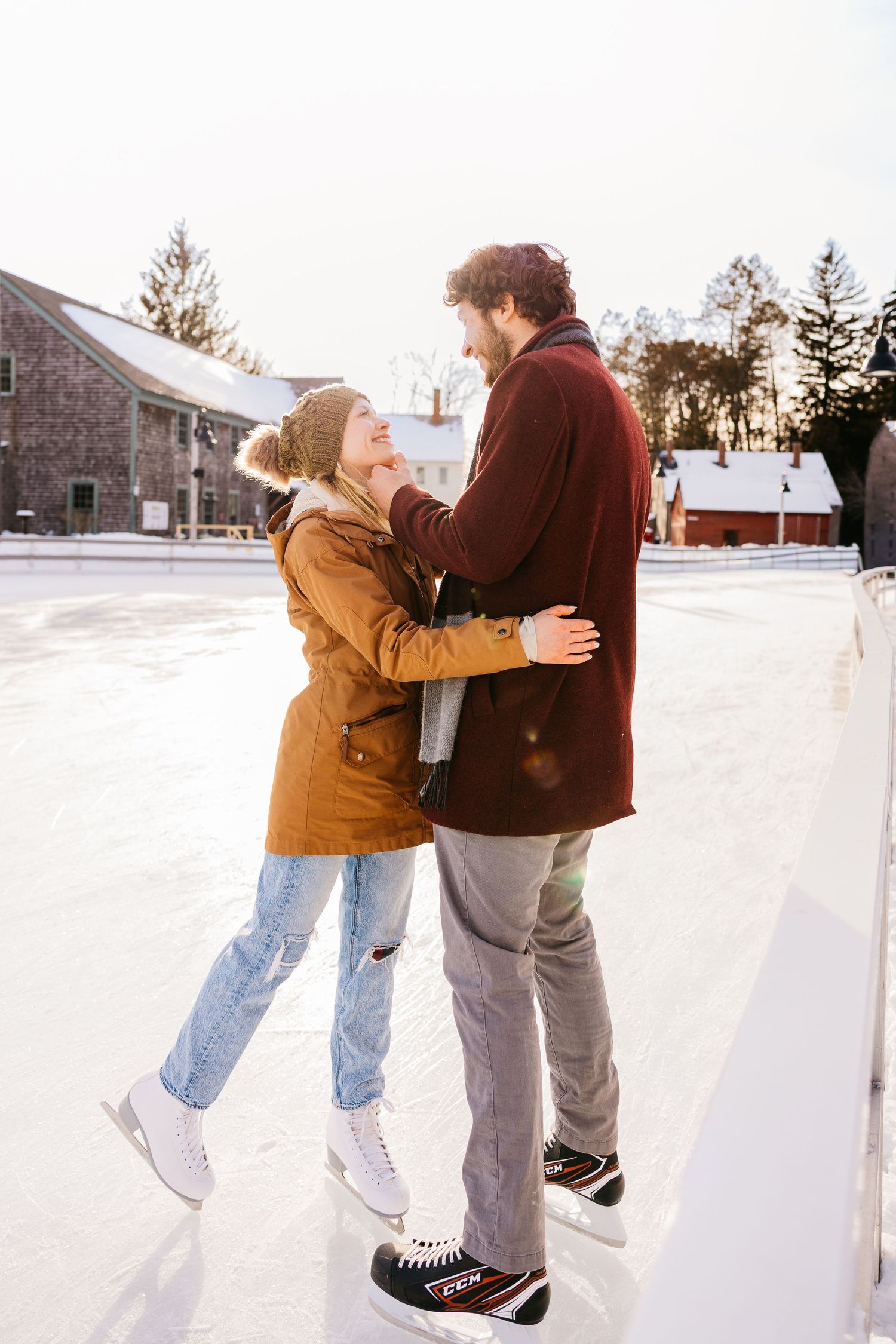 A couple ice skating together at an outdoor rink on a winter day, wearing warm coats and holding each other close.