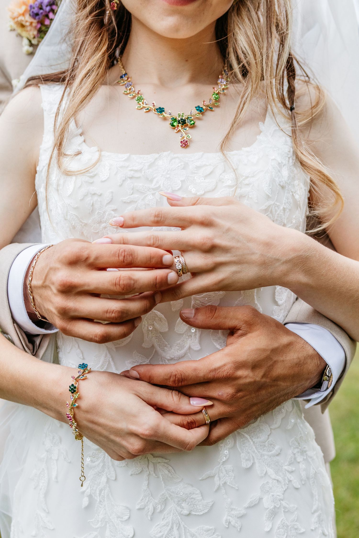 Close-up views of hands wearing delicate jewelry and white lace dress details in an outdoor setting.