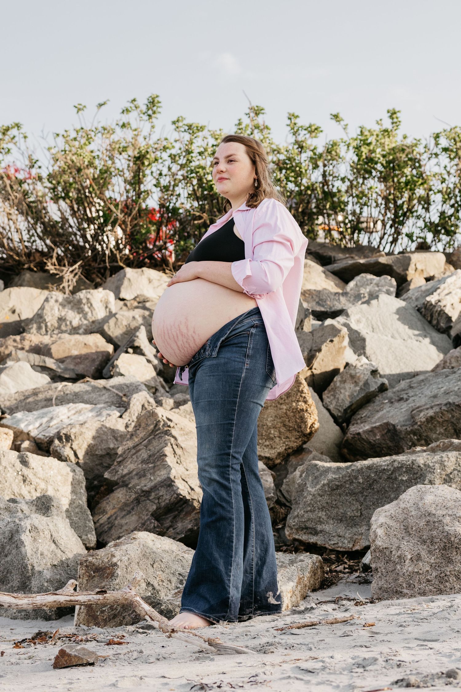 Maternity photoshoot on rocky beach with pink shirt and overalls.