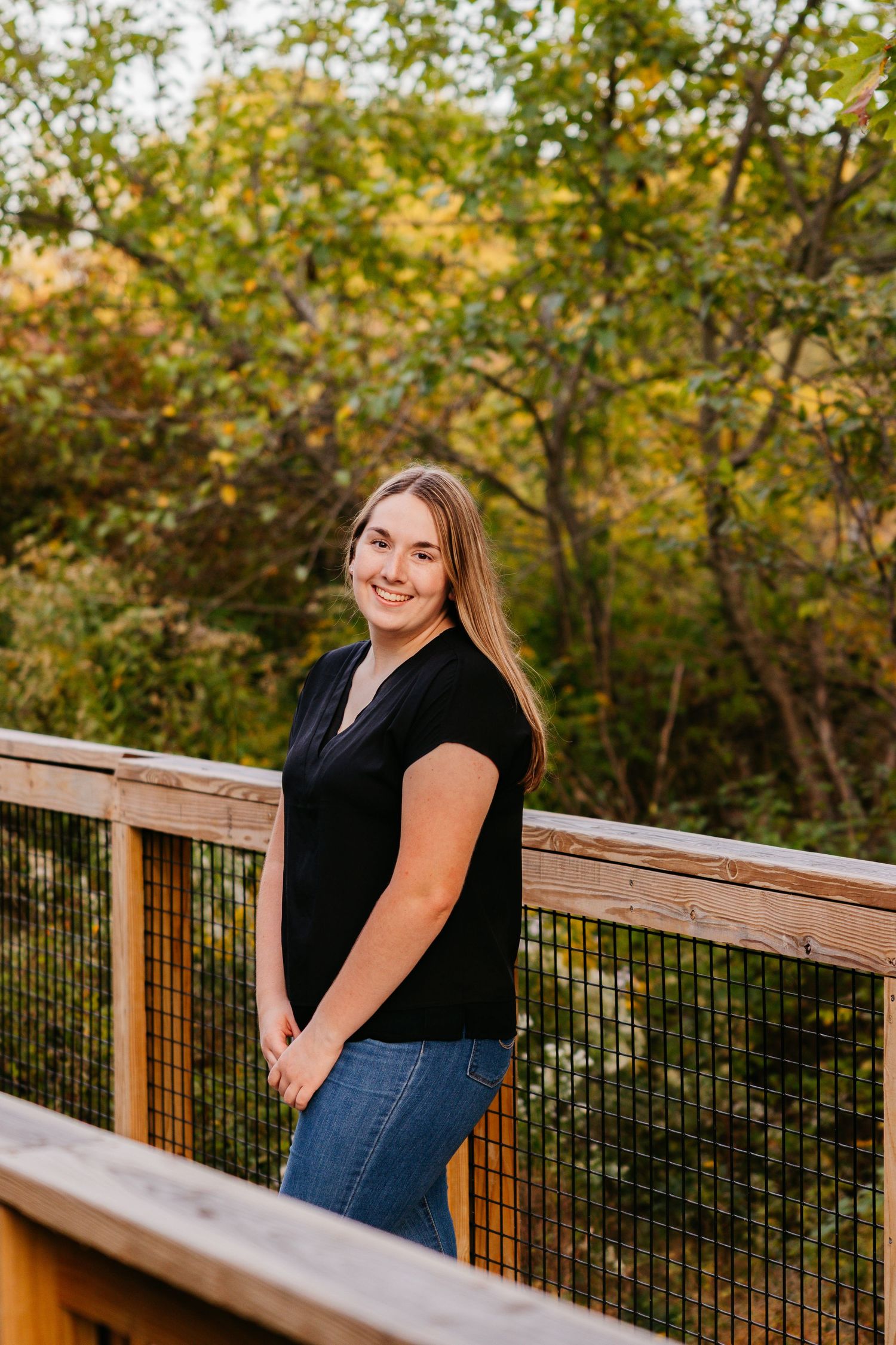 Wooden deck railing overlooks autumn trees and natural scenery at golden hour.