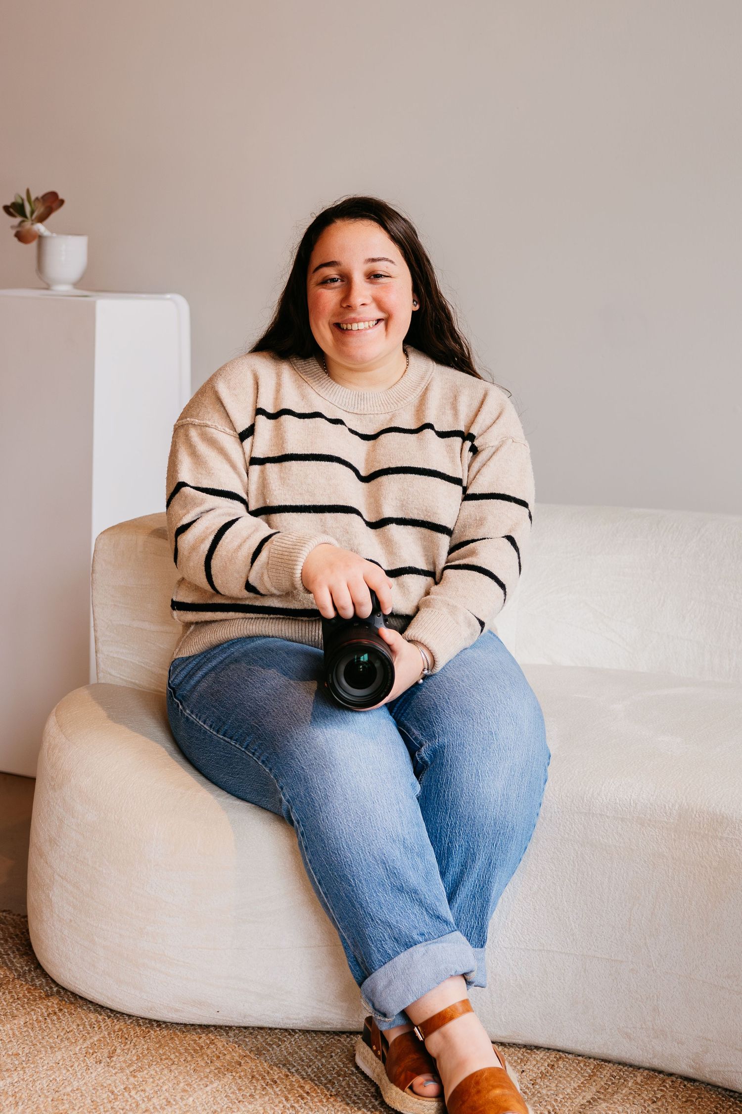 A person in a striped sweater and jeans sits comfortably in a beige bean bag chair against a light-colored wall.