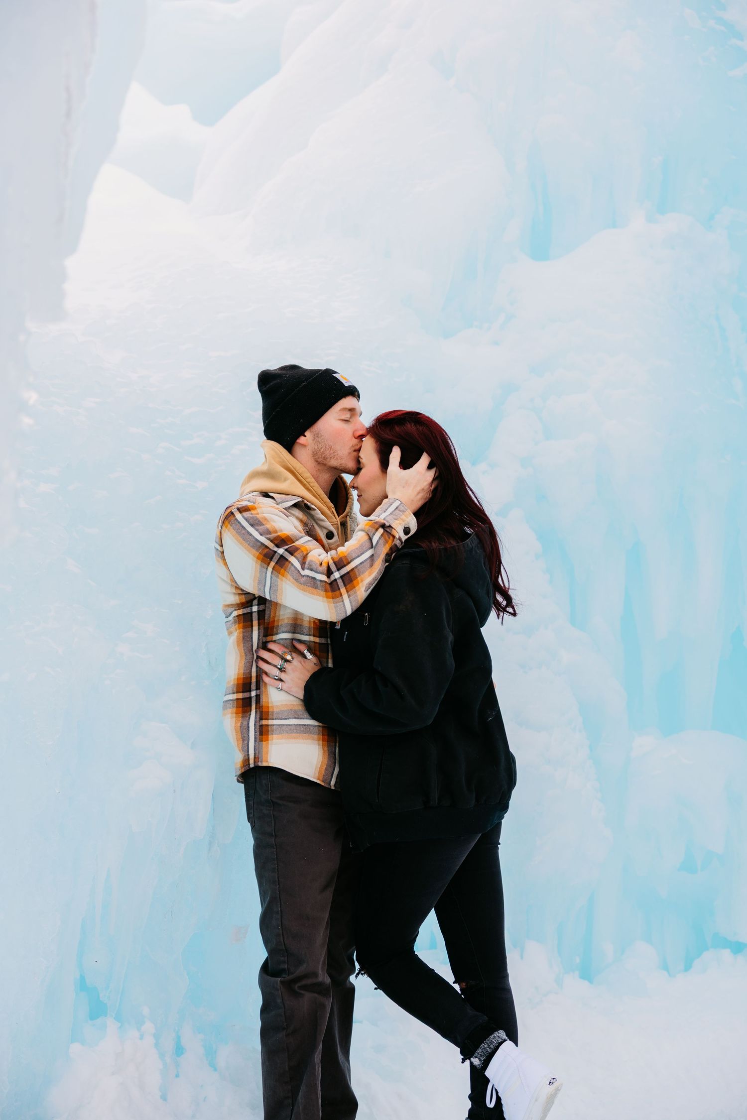 A couple shares a romantic moment against an ethereal blue ice cave backdrop during a winter photo session.