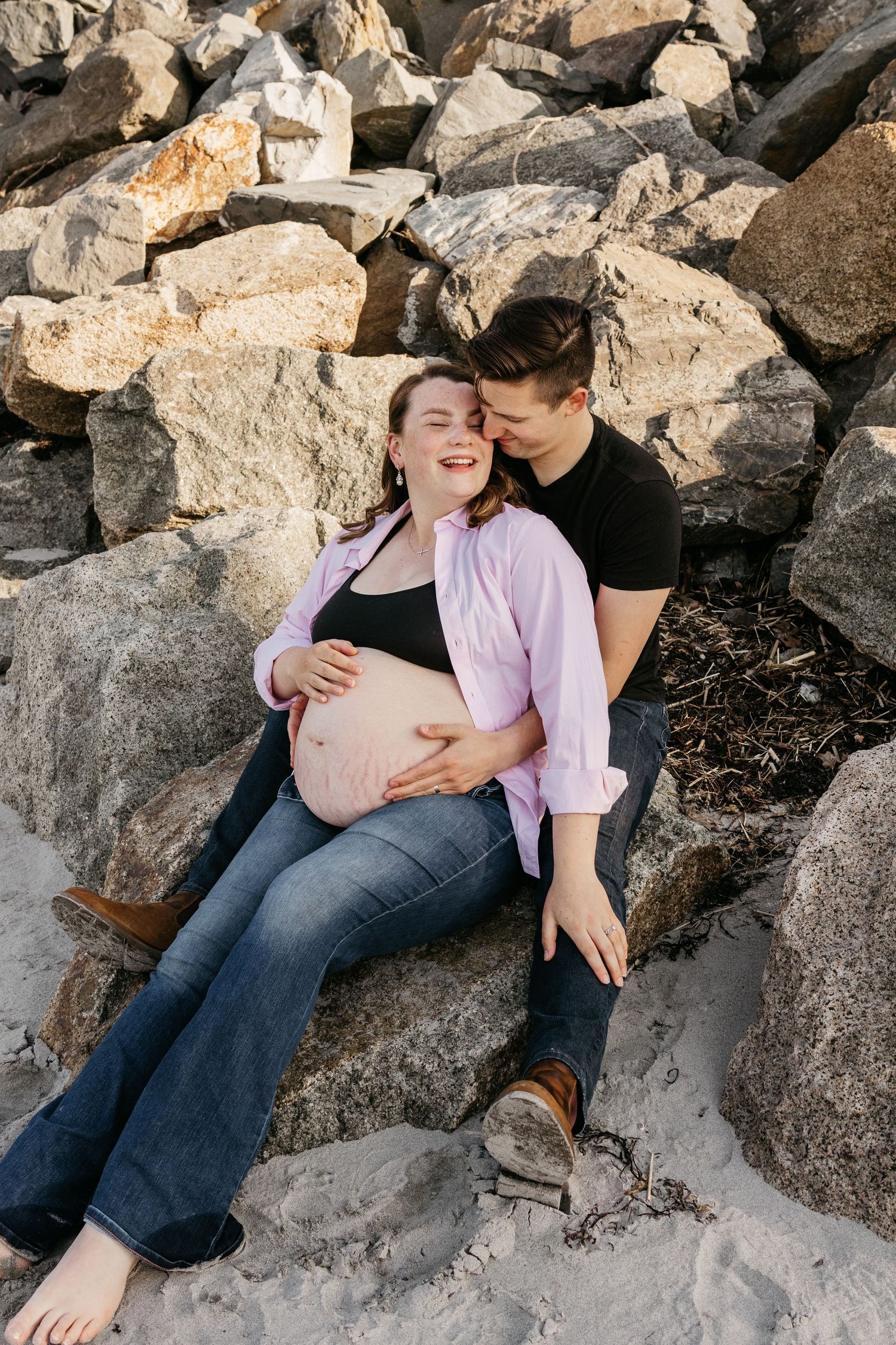 Couple sharing intimate moment while sitting on coastal rocks.