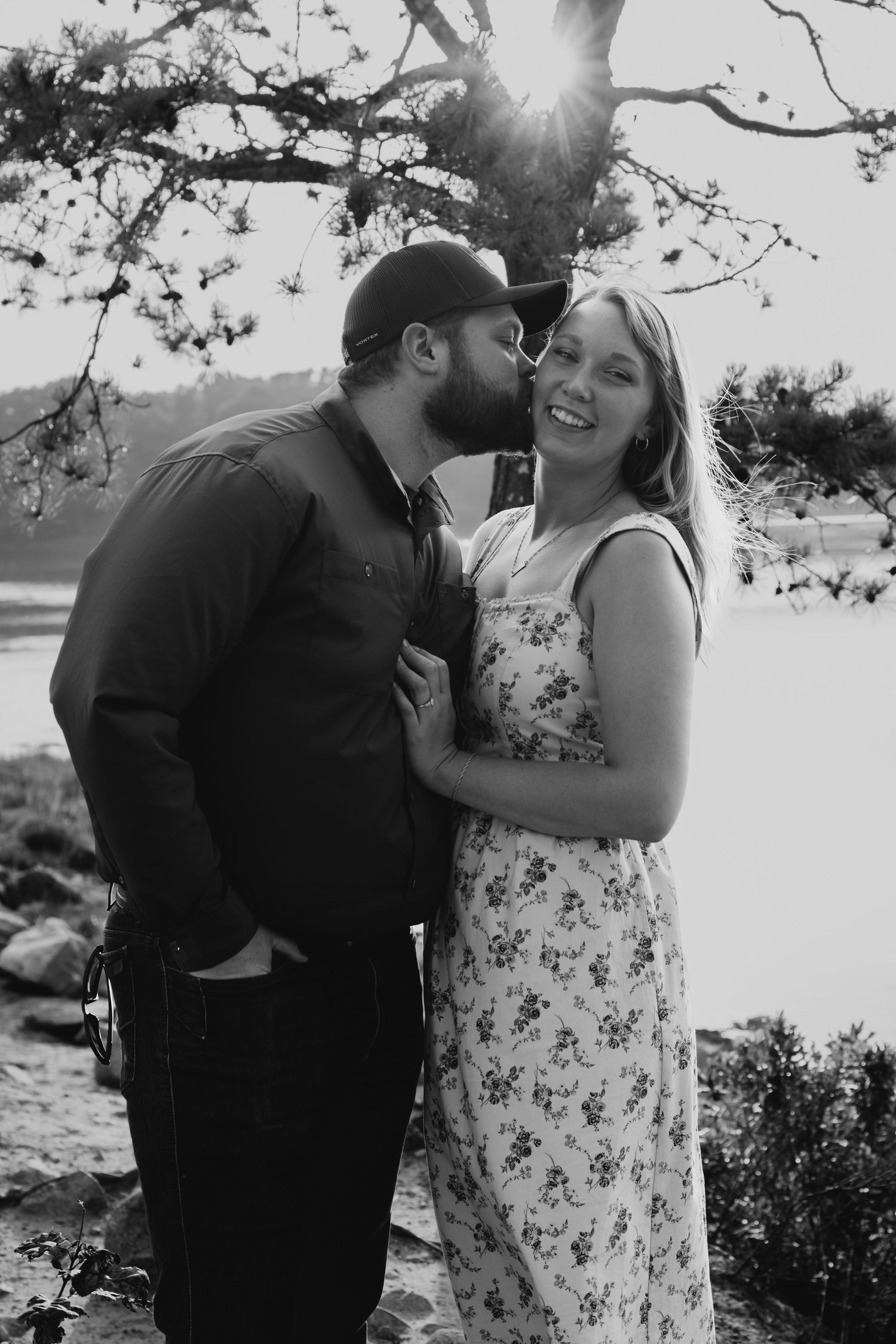 Couple sharing intimate moment outdoors under tree branches in black and white photo.