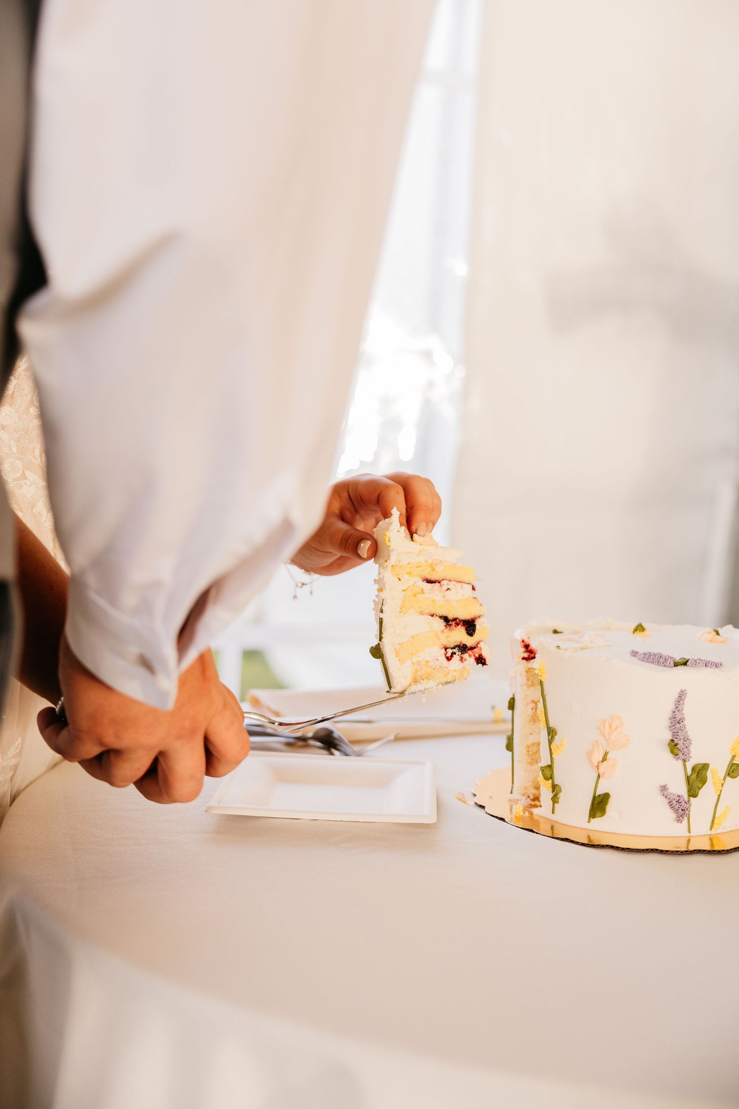 Couple cutting a floral decorated white wedding cake at their reception ceremony.