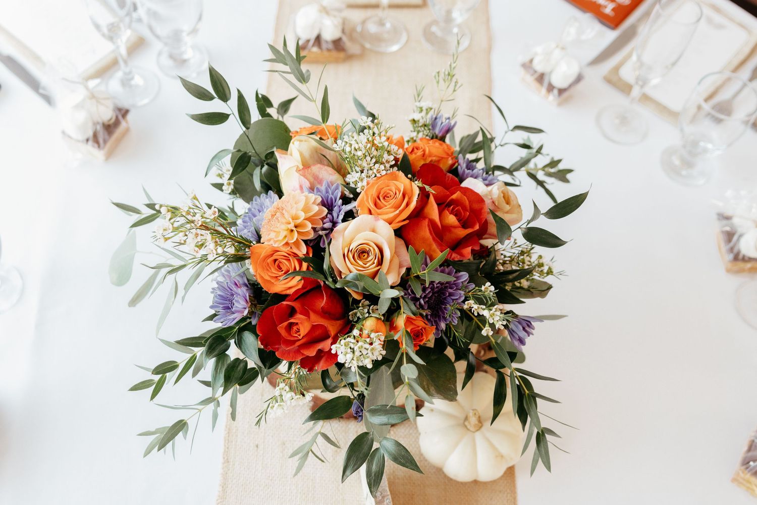 Vibrant floral arrangement with orange and red roses mixed with purple flowers and eucalyptus.