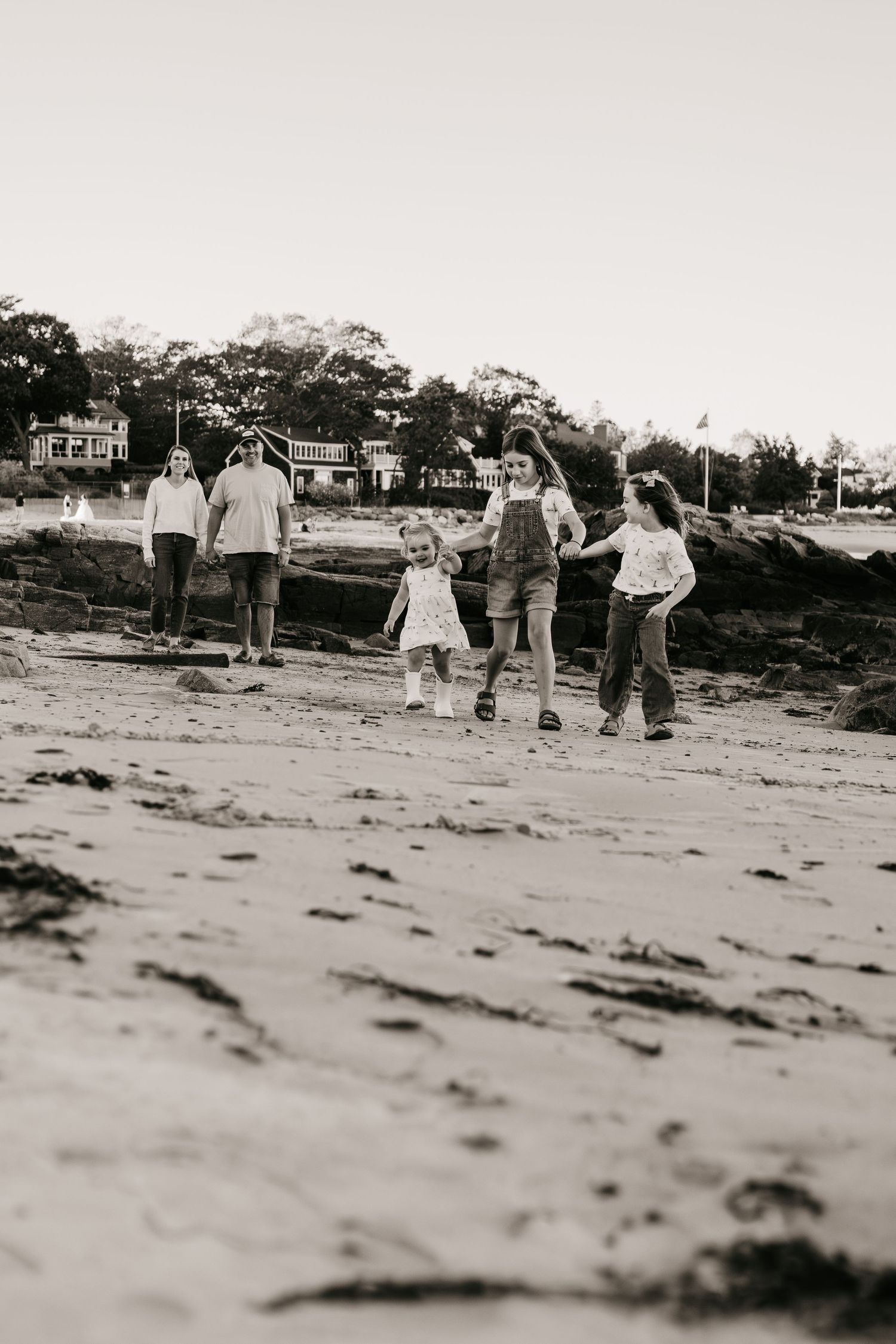 Black and white sequence showing people playing and running on a sandy beach with houses visible in background.