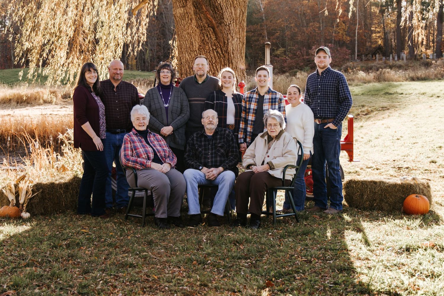 Multi-generational group portrait outdoors in autumn with hay bales and fall foliage in the background.