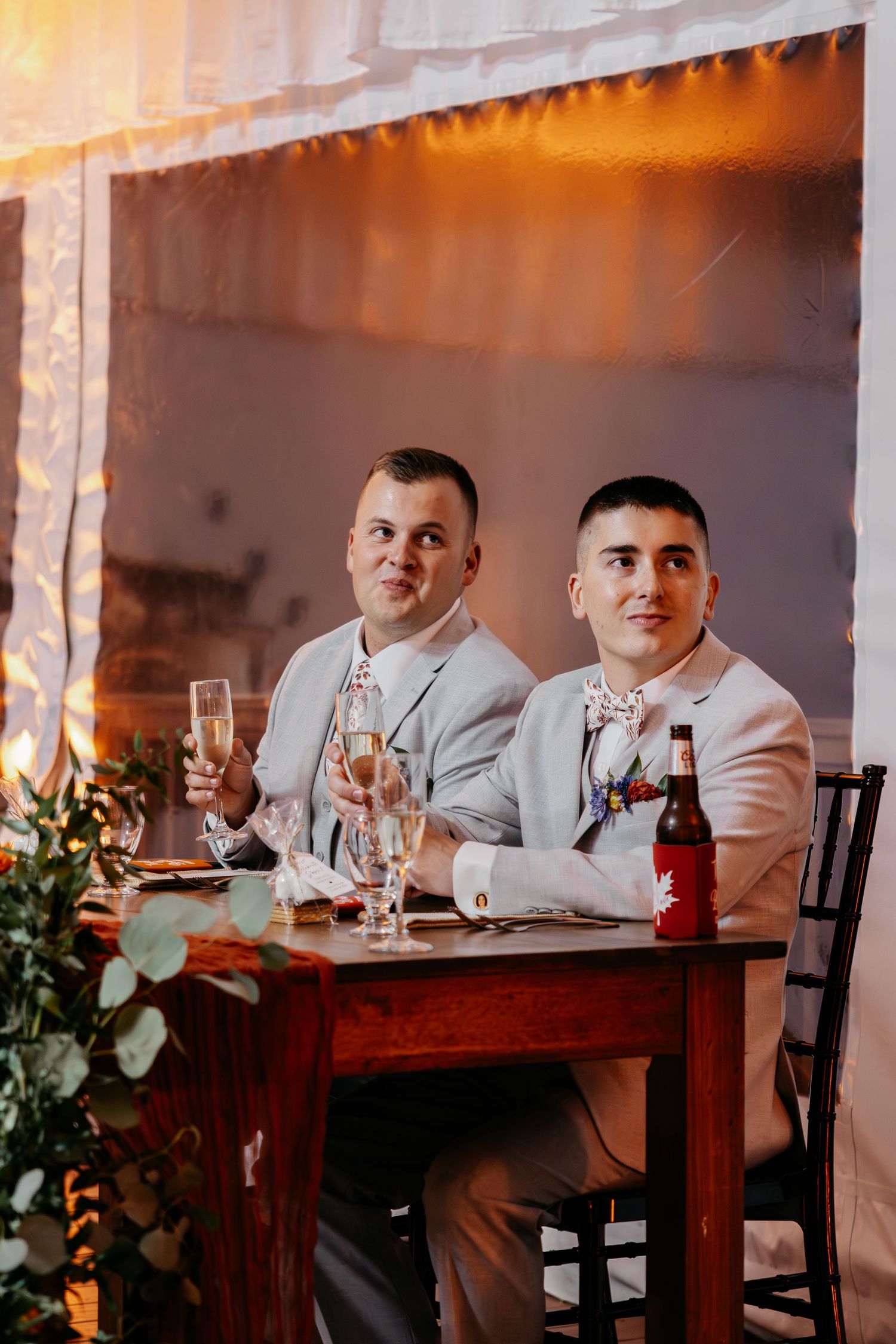 Wedding guests seated at a rustic wooden table with elegant table settings and greenery decor.
