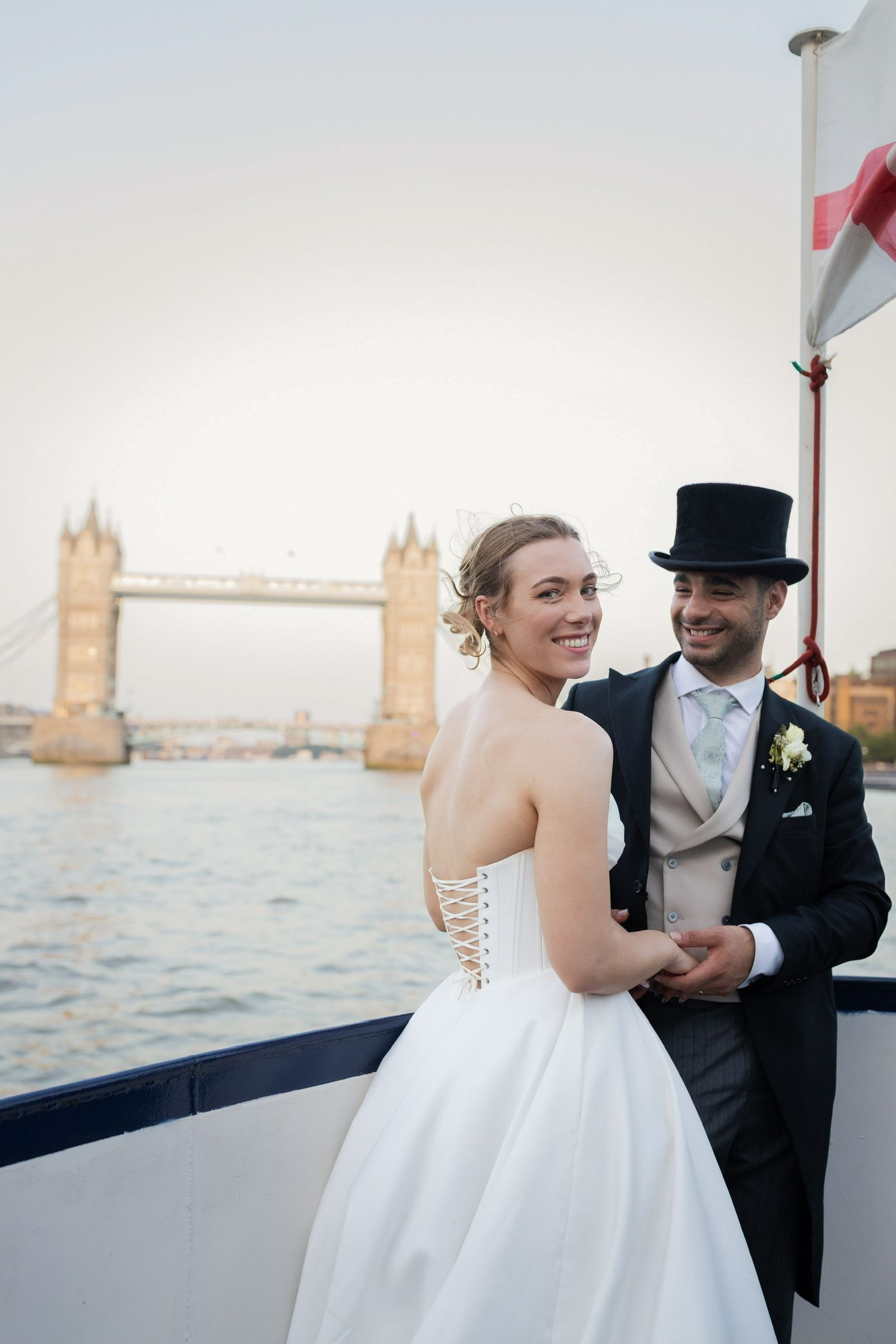 Bride and groom posing on a boat with Tower Bridge London in the background at sunset.