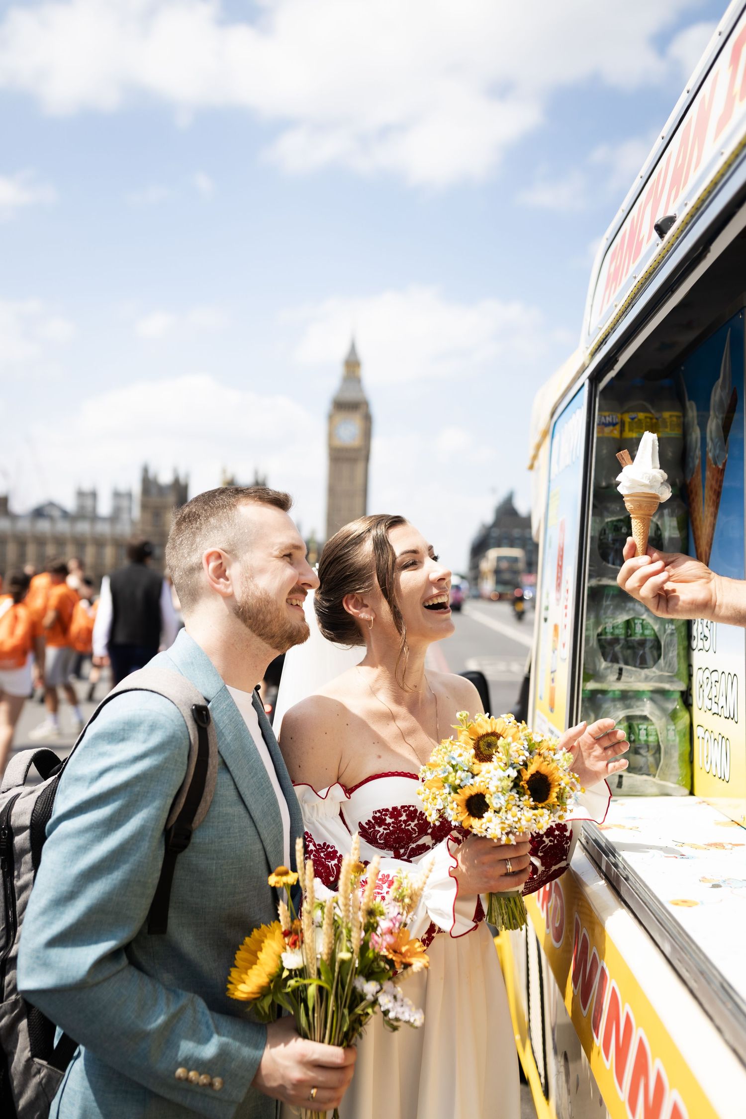 Newlyweds buying ice cream from a street vendor near Big Ben in London, bride holding sunflower bouquet.