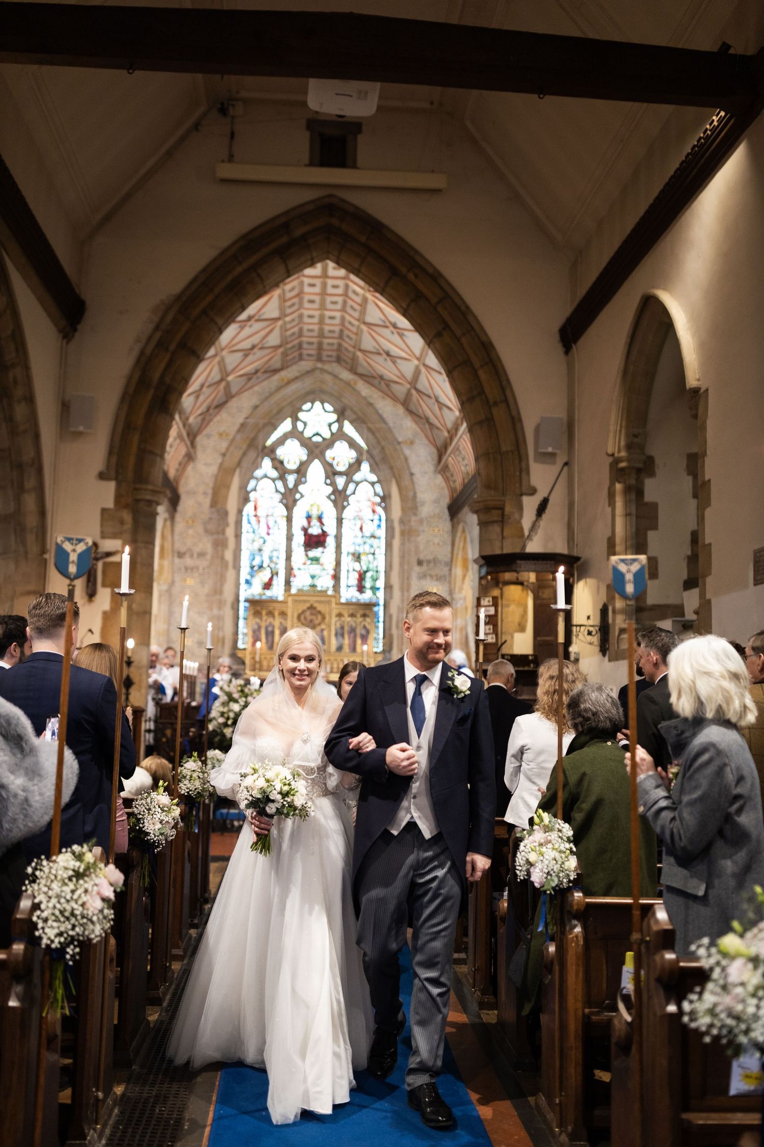 Bride and groom walk down the aisle of a stunning stone church after their wedding ceremony.