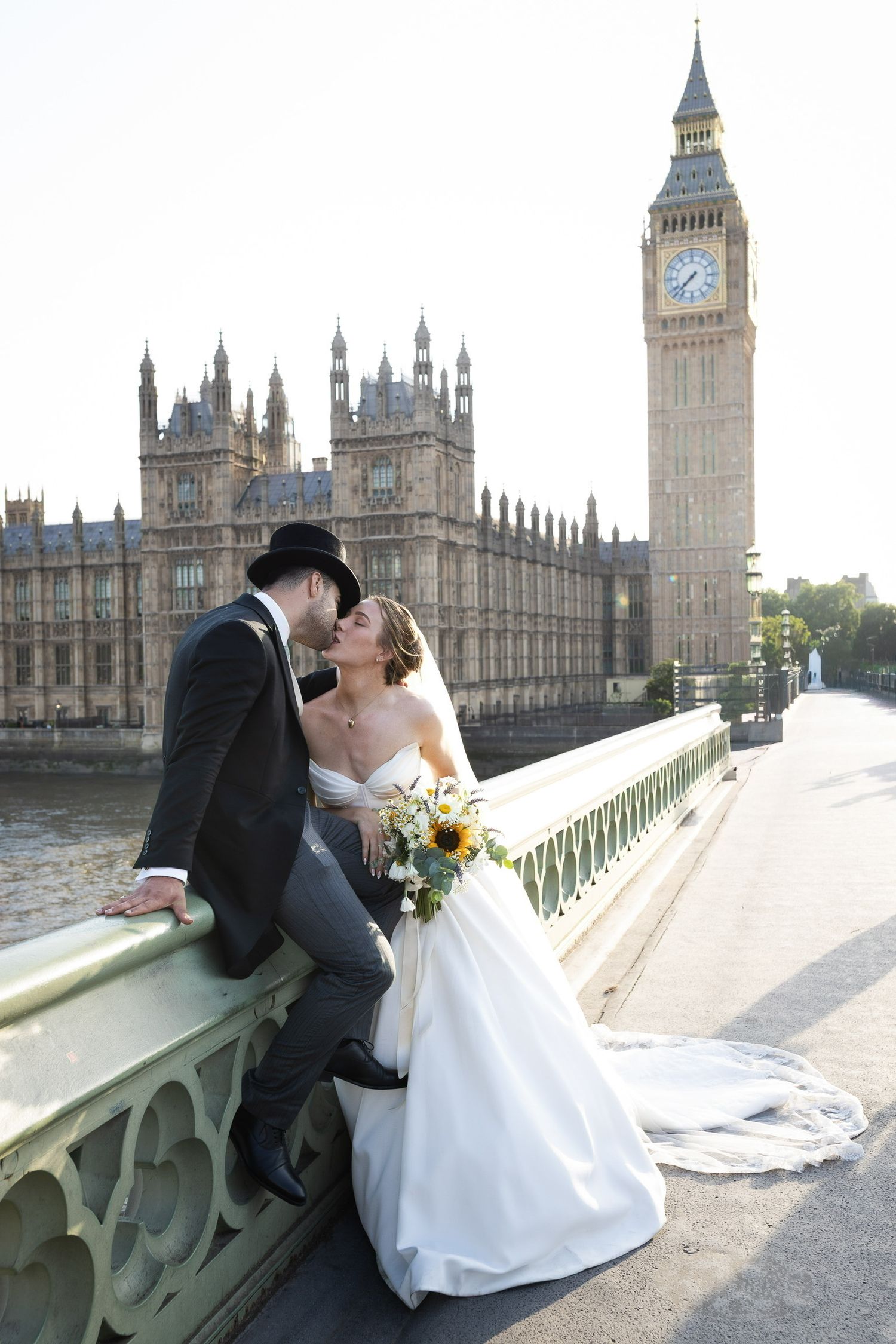 Bride and groom kissing on Westminster Bridge with Big Ben and Houses of Parliament in London backdrop.