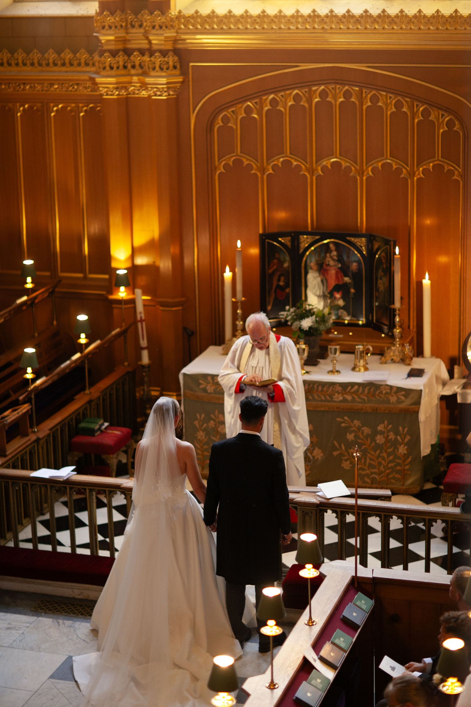 Bride and groom stand before an officiant at a candlelit church altar during a traditional wedding ceremony.