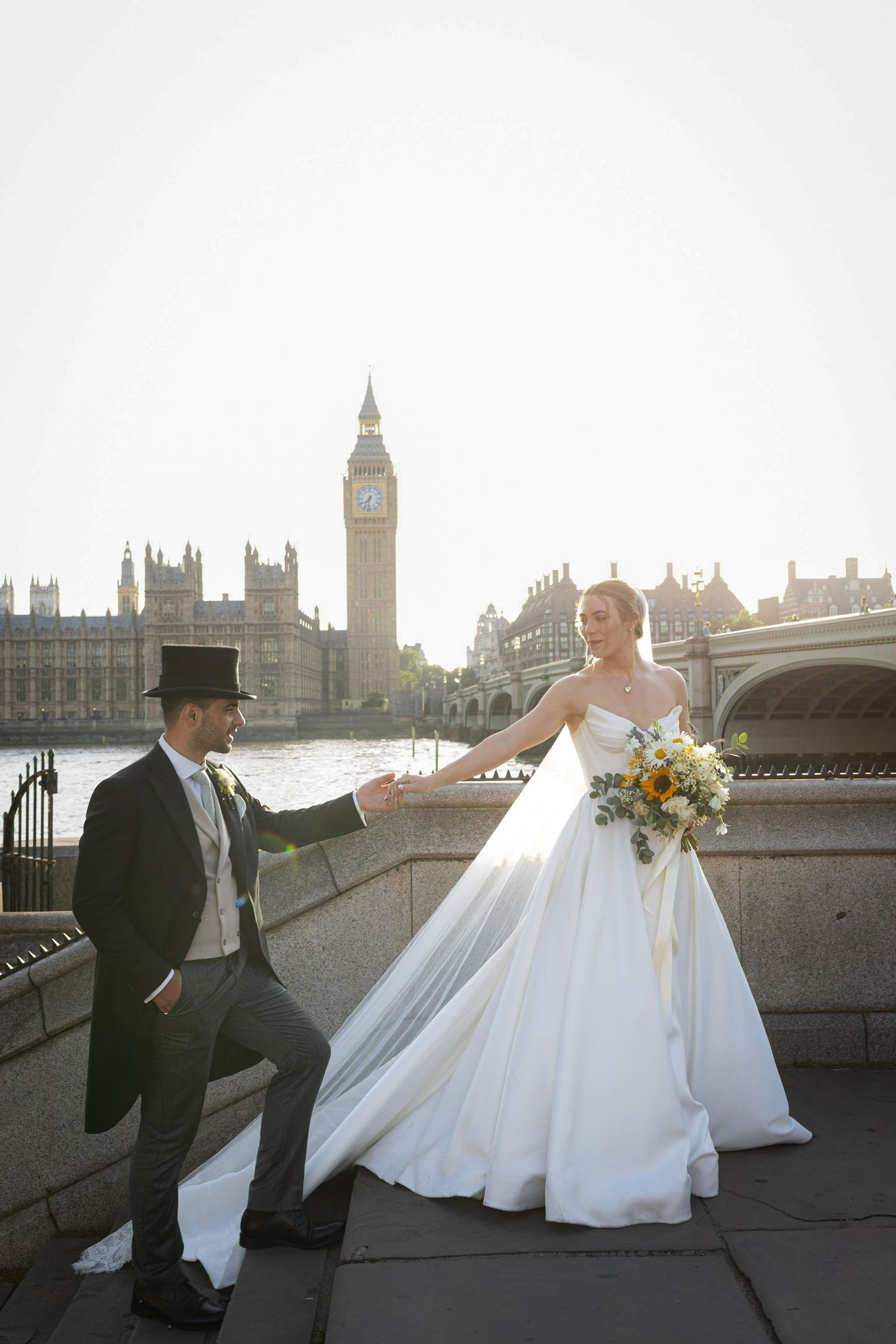 Bride and groom holding hands near Big Ben and Westminster Bridge in London on their wedding day.